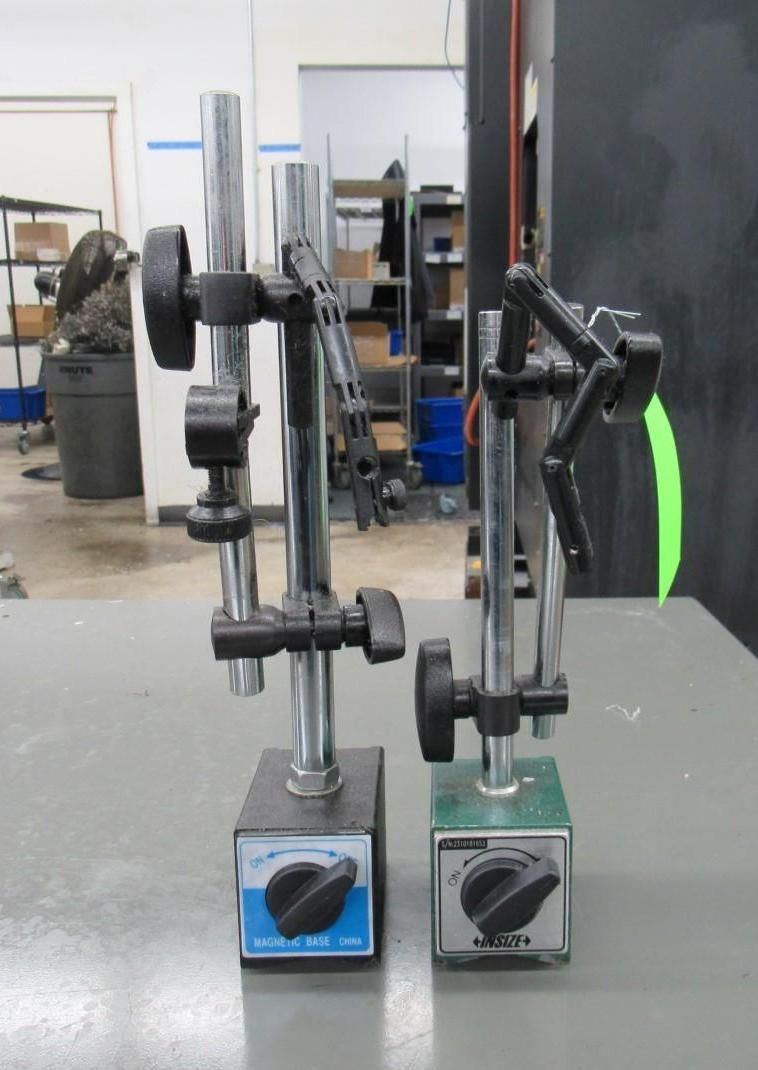 Two magnetic base dial indicator holders on a gray tabletop in a workshop.