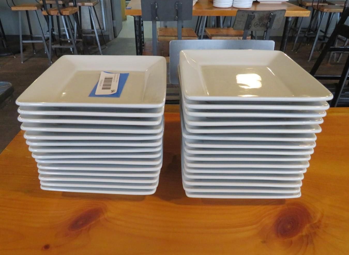 Two stacks of square, cream-colored plates on a wooden table.