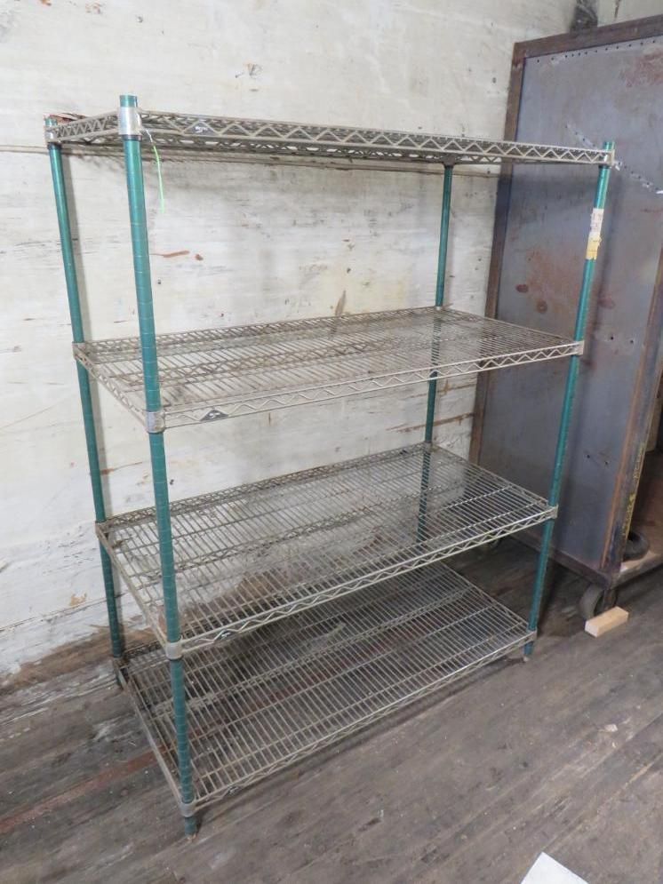 Metal wire shelving unit with four levels, teal posts, in front of a concrete wall.