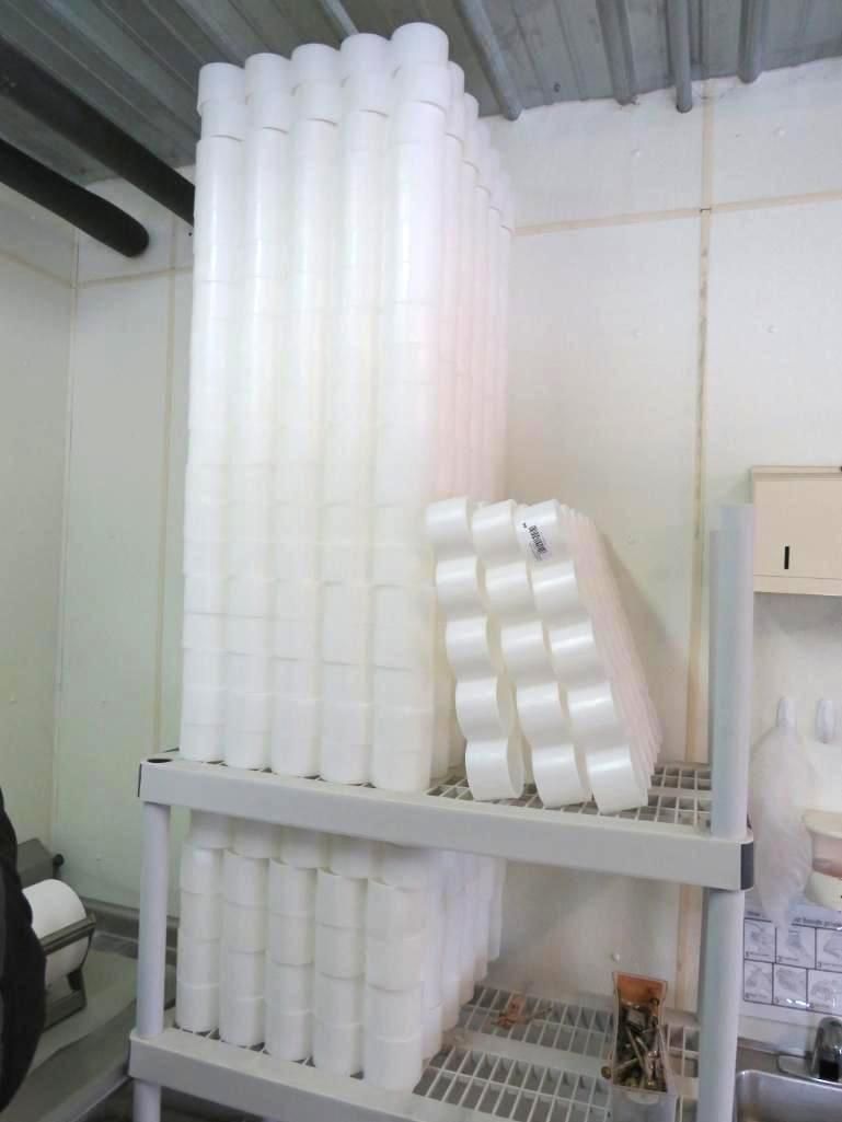 Stacks of white disposable cups on shelves inside a utility closet.