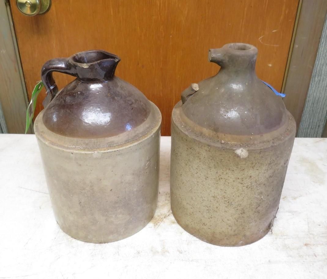 Two stoneware jugs, one with a handle and dark brown top, the other with a spout, both tan-colored.