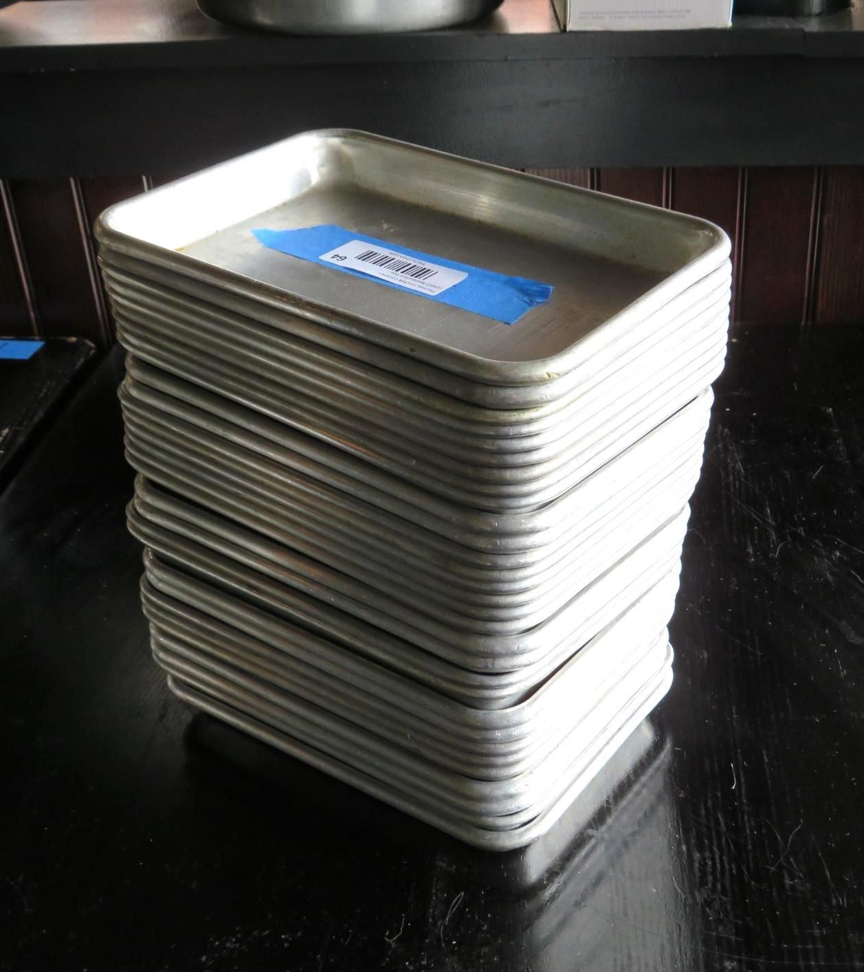 Stack of rectangular metal trays on a dark surface, one labeled with blue tape.