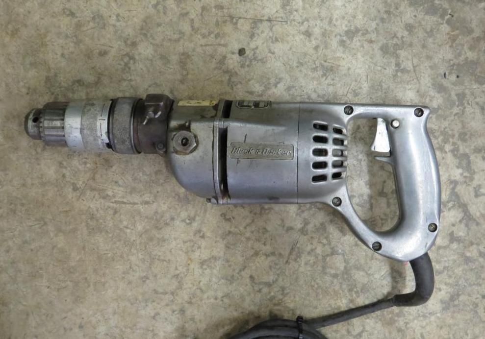 Silver electric drill with a black cord on a concrete surface.