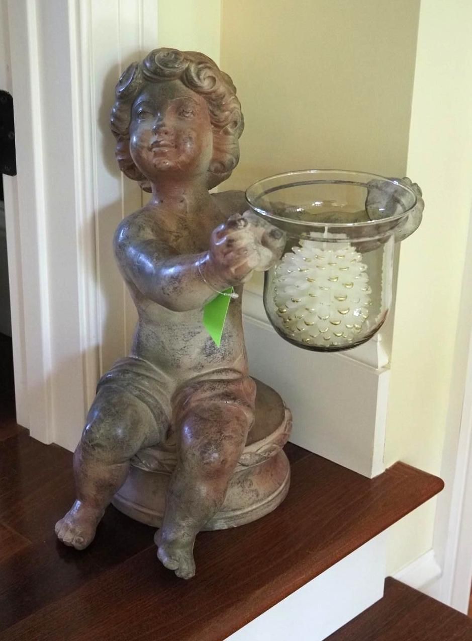 Statue of a cherubic figure holding a glass container on a wooden step; aged appearance.