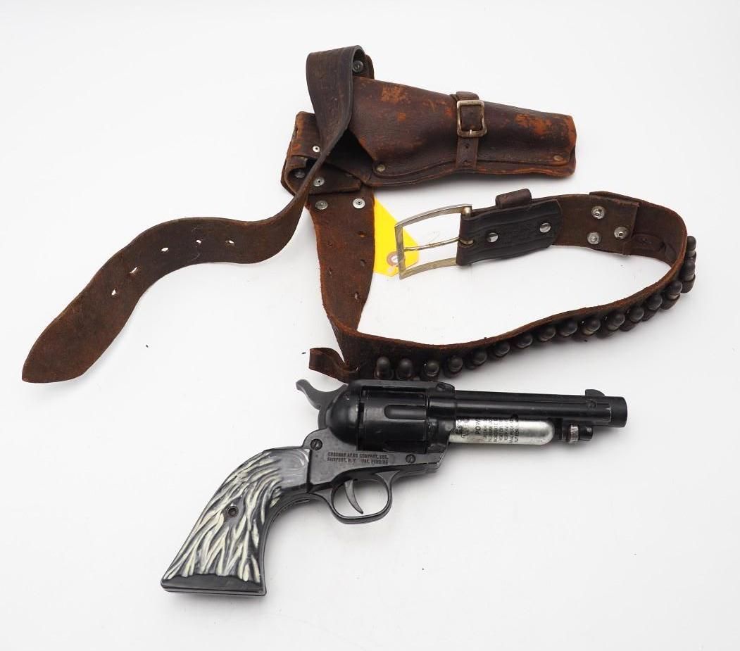 Black revolver with silver grip beside a brown leather holster and belt on a white background