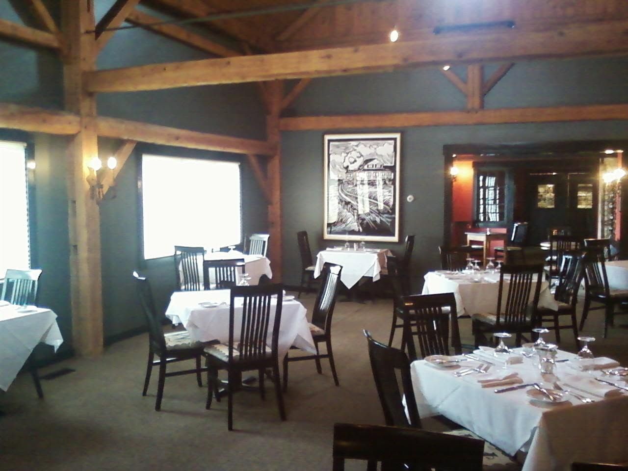 Rustic restaurant dining room with wooden beams, tables, chairs, and white tablecloths