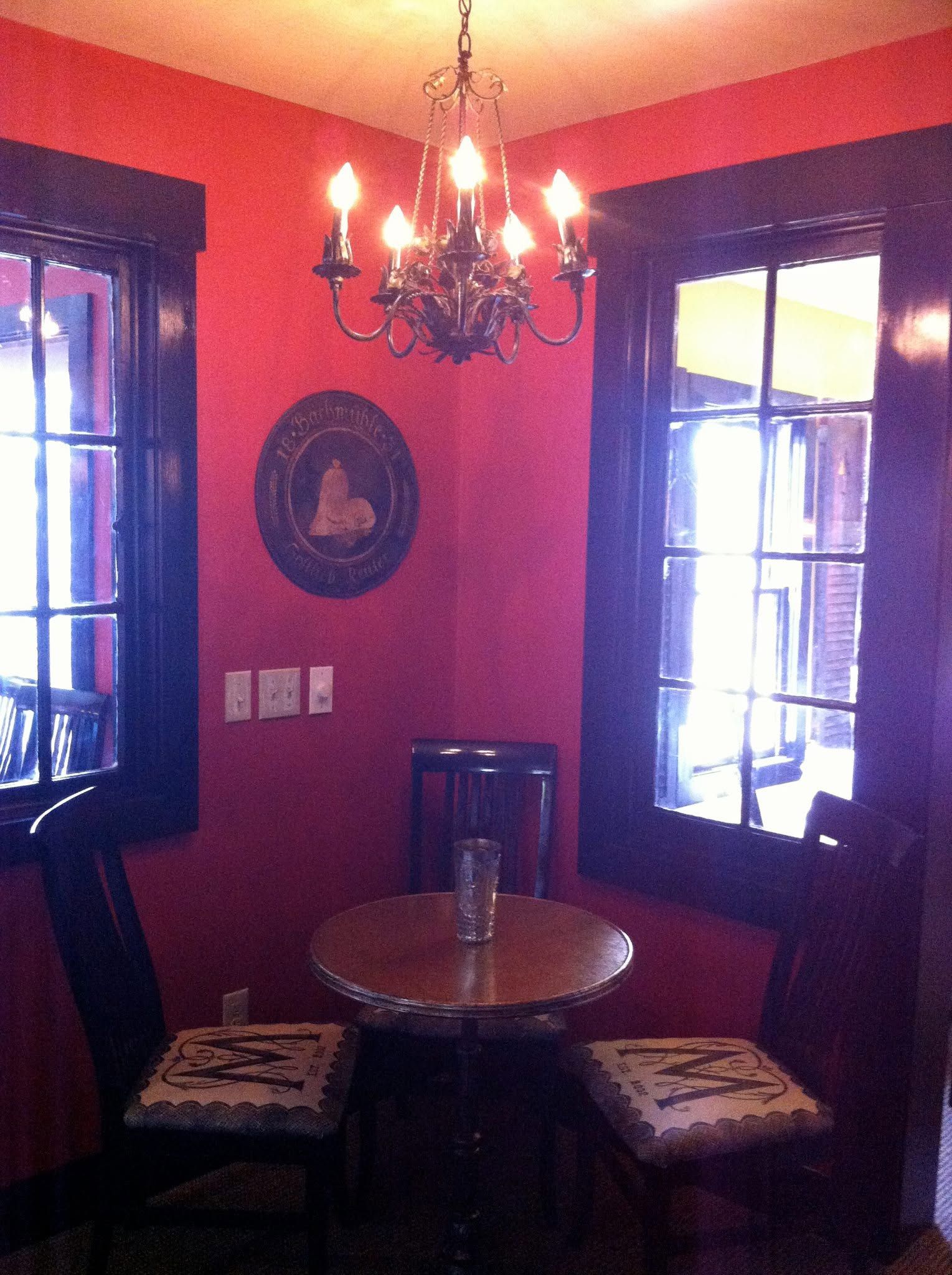 Cozy corner with red walls, chandelier, small round table, and two window benches.