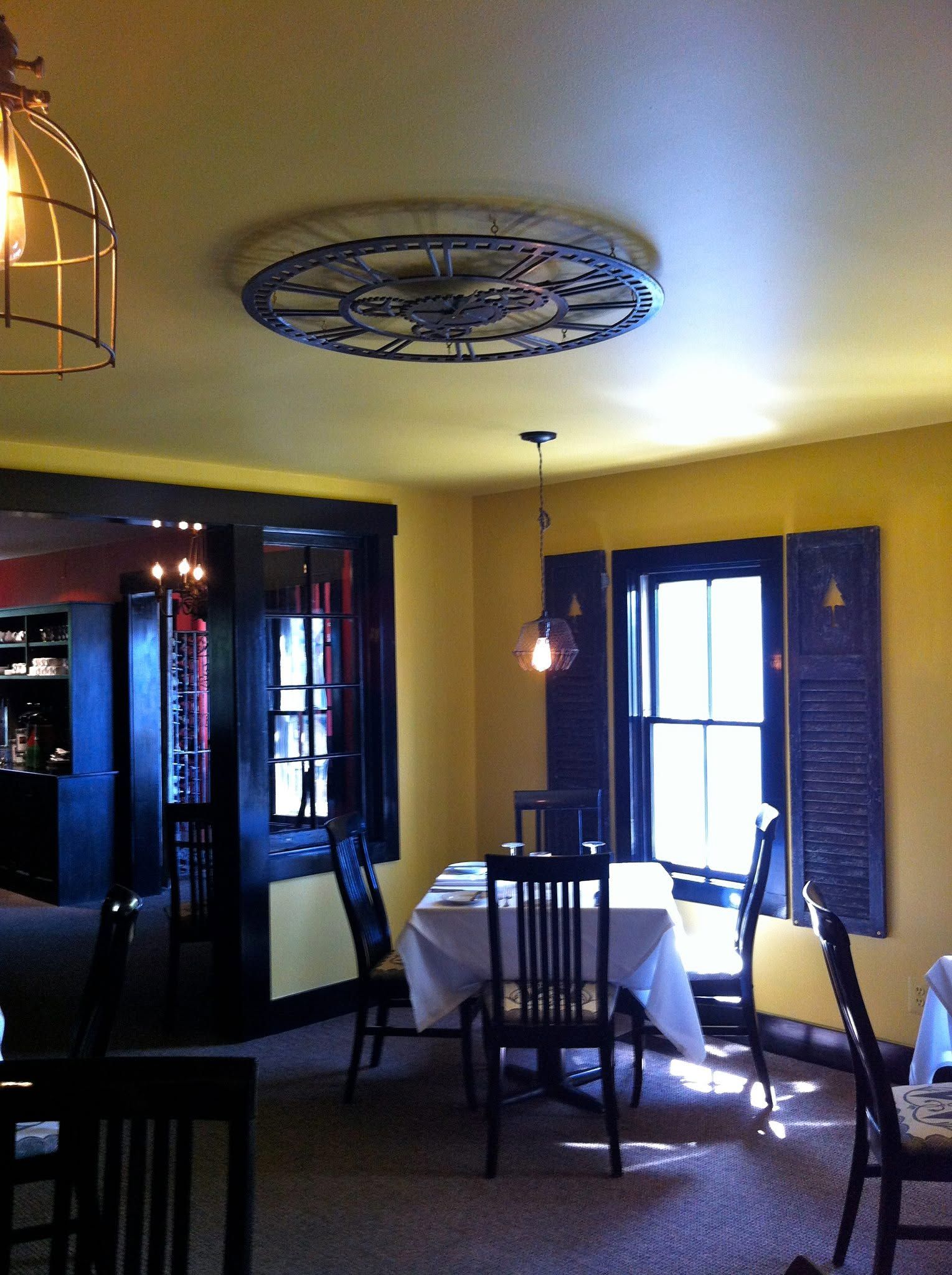 Restaurant interior with yellow walls, blue shutters, tables, and chairs under decorative ceiling lights