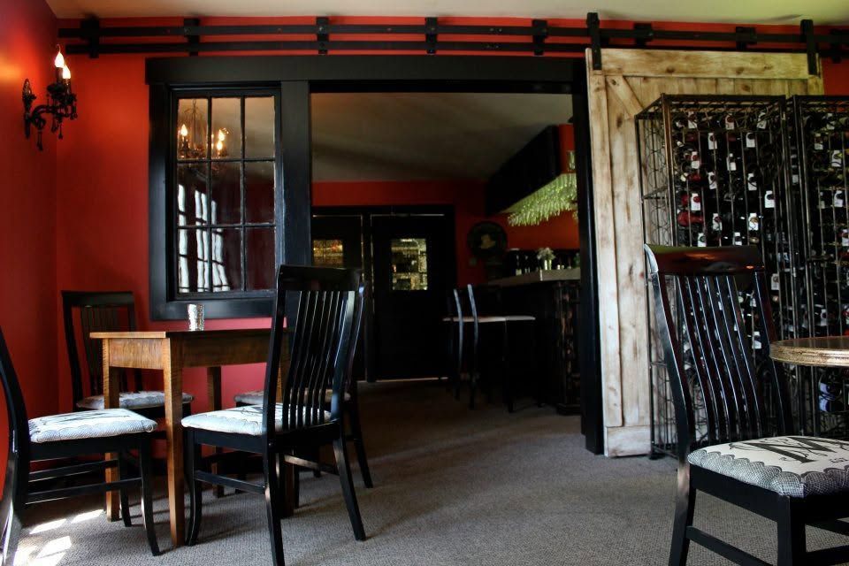 Red-walled restaurant interior with dark chairs, wooden tables, and a doorway to a dining area