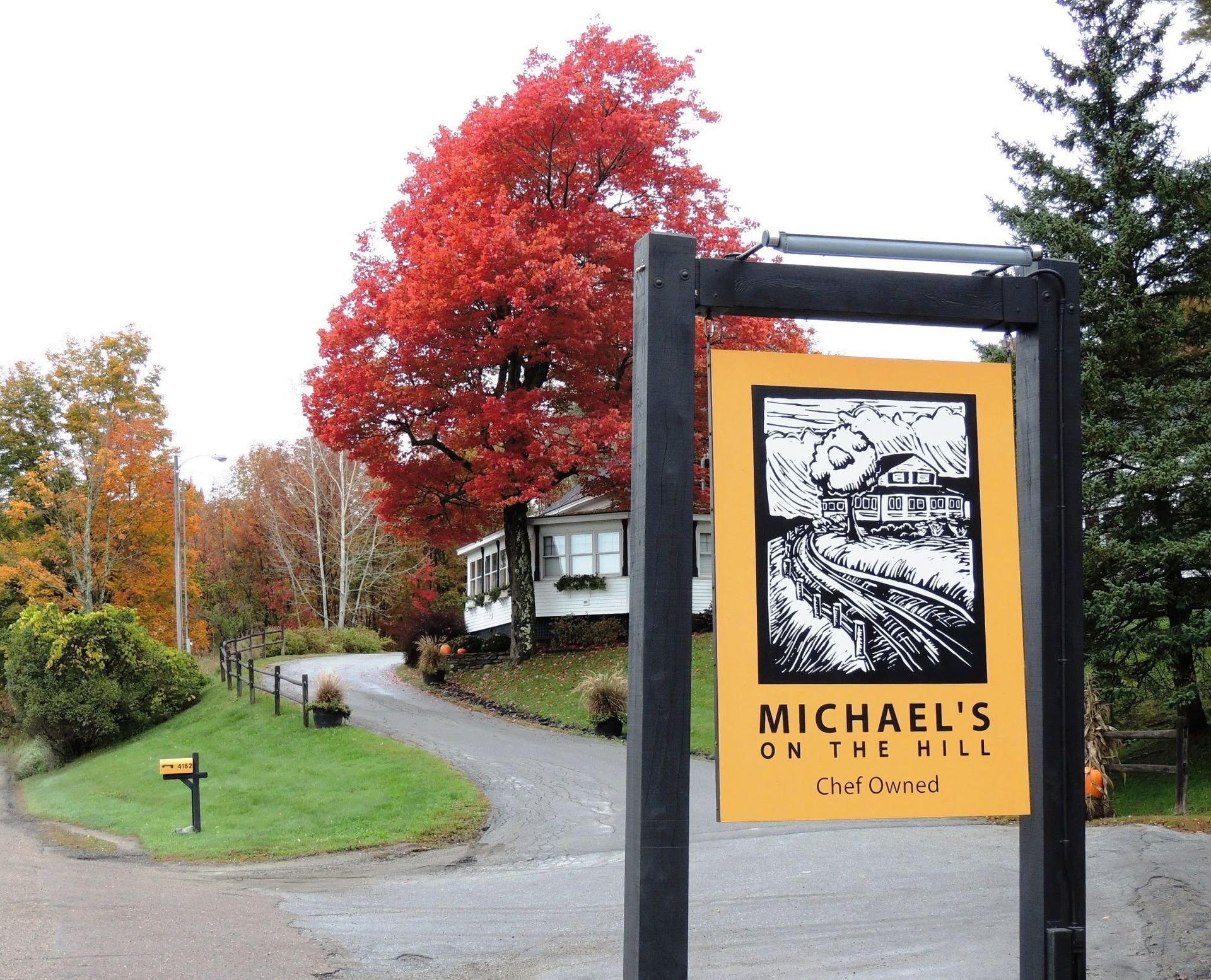 Sign for Michael’s on the hill, beside a curving driveway and a red autumn tree