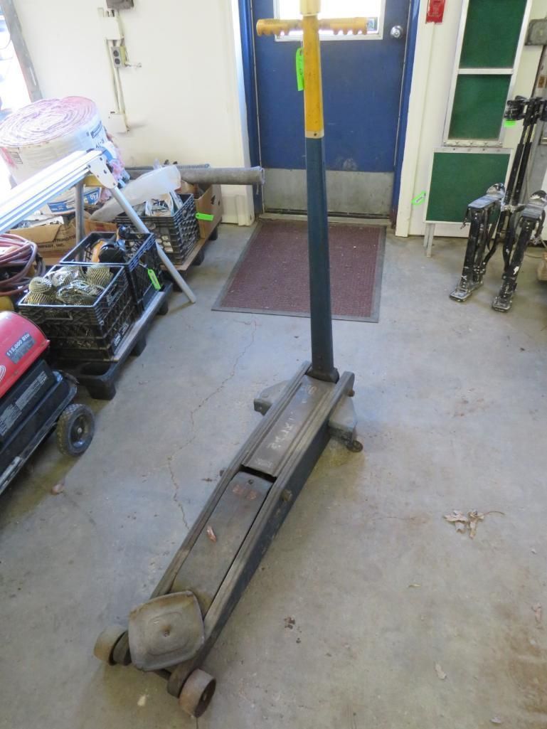 Floor jack with yellow handle, in a garage.