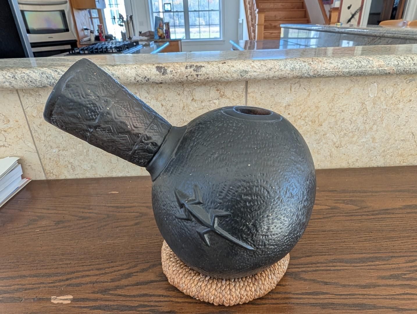 Black ceramic vase with a narrow neck on a woven coaster on a wooden counter indoors