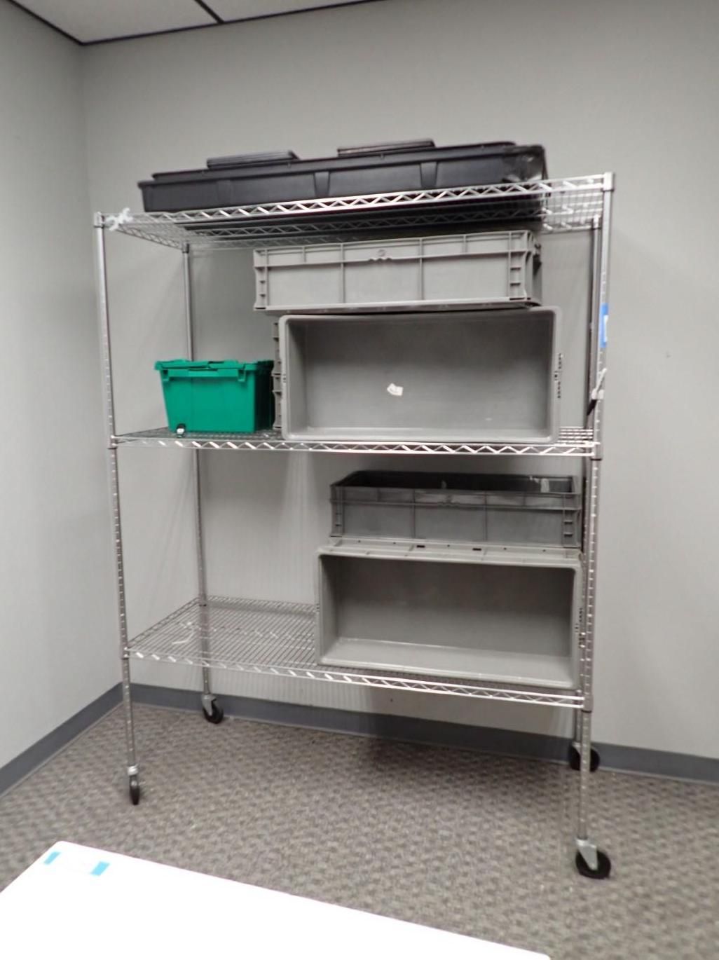 Metal shelving unit on wheels holding various storage containers in a room with light gray walls.