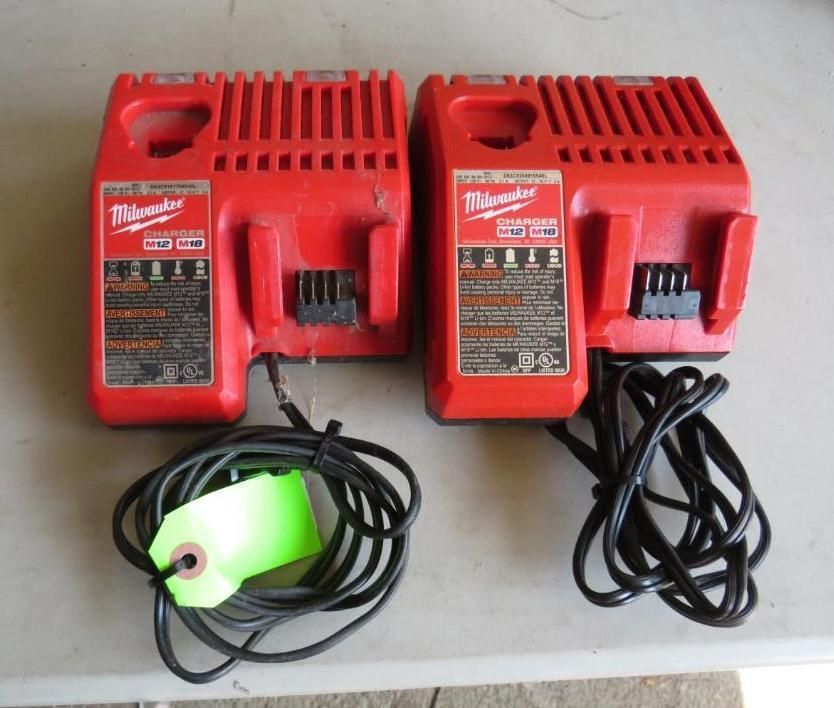 Two red Milwaukee M18 battery chargers with black cords, set on a light surface.