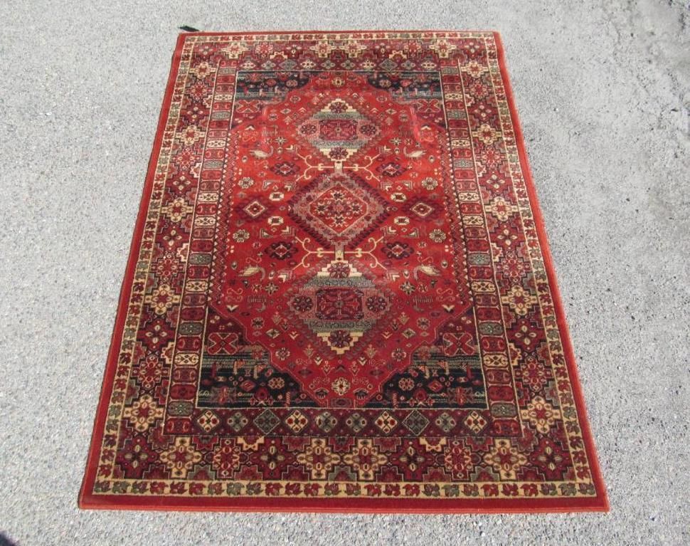Red and beige patterned oriental rug on a gray surface.