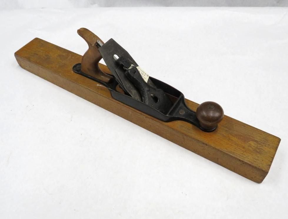 Wooden hand plane, brown and black, with a handle, sitting on a white surface.