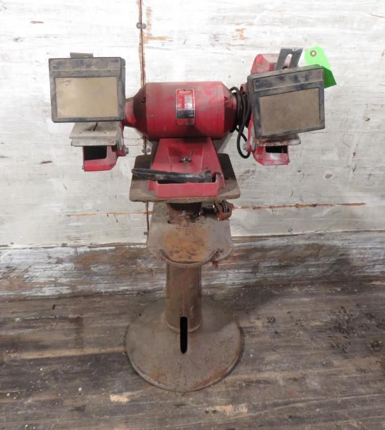 Red bench grinder on a pedestal stand; two grinding wheels with safety shields.