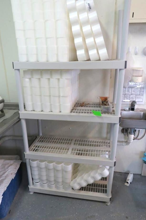 White plastic shelving unit with various containers and items in a workshop setting.
