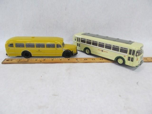 Two toy buses, one yellow and one cream, sit on a white surface next to a ruler.