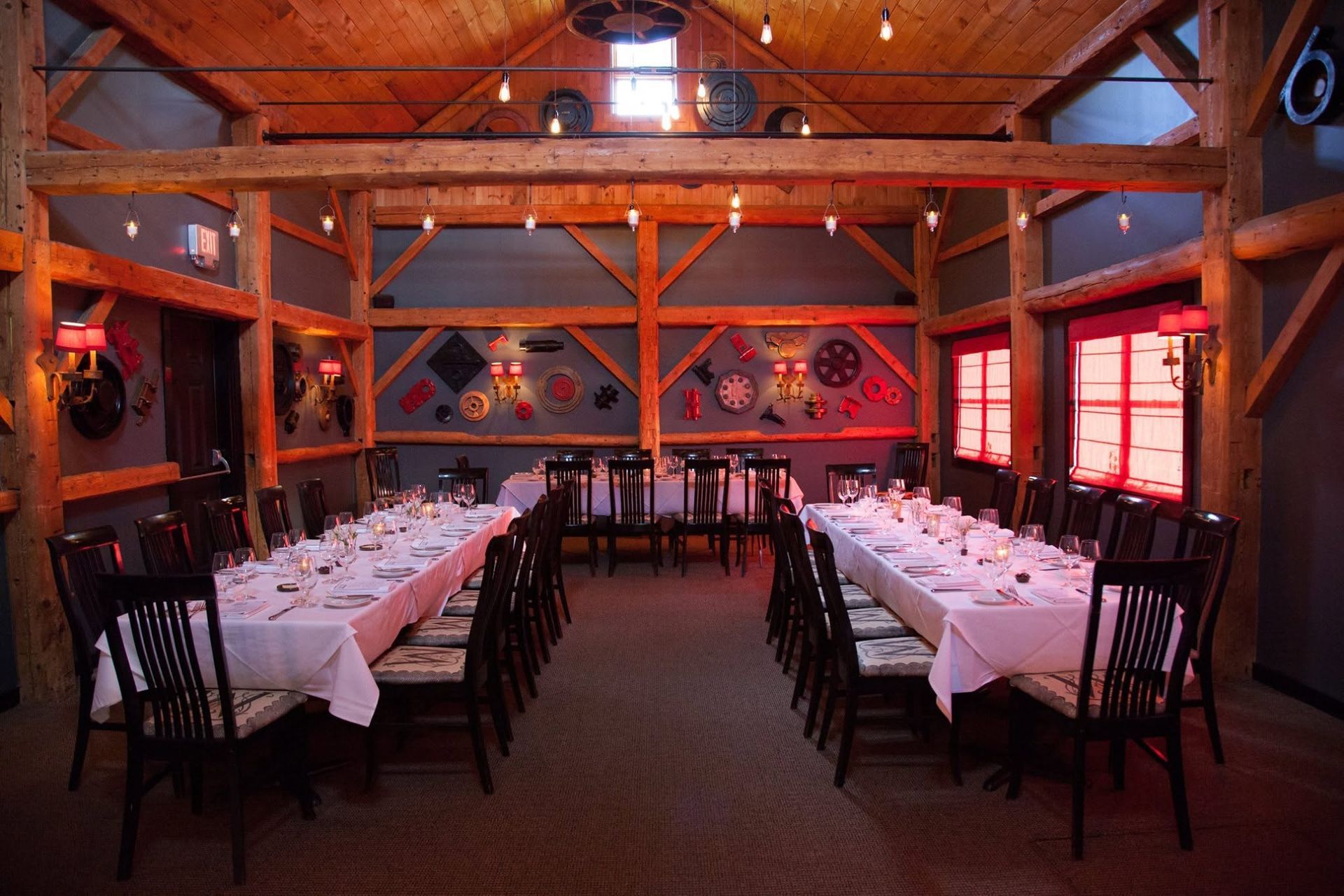 Rustic banquet hall with long set tables, wooden beams, and red window light