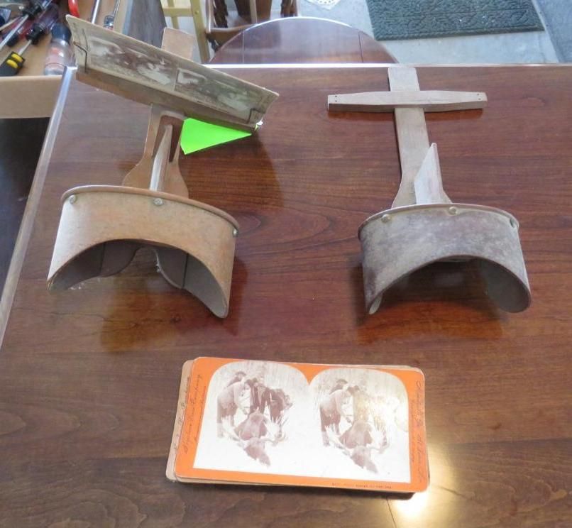Two antique stereoscopes and a stereoview card on a wooden table.