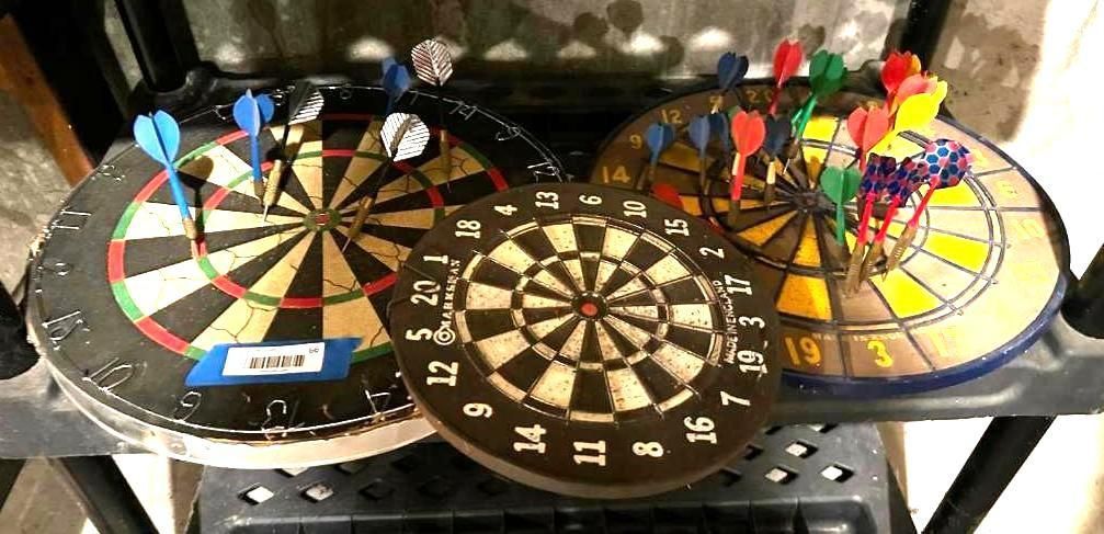 Three dartboards on a shelf with darts stuck in them.