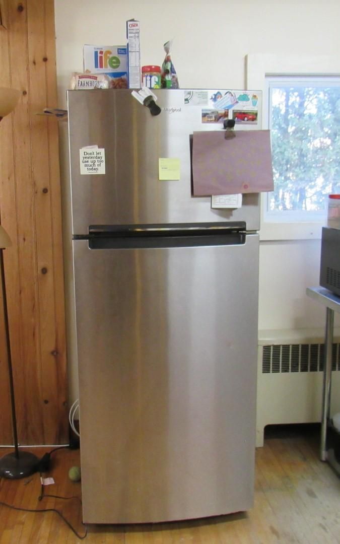 Stainless steel refrigerator in a kitchen setting with magnets, notes, and a window in the background.