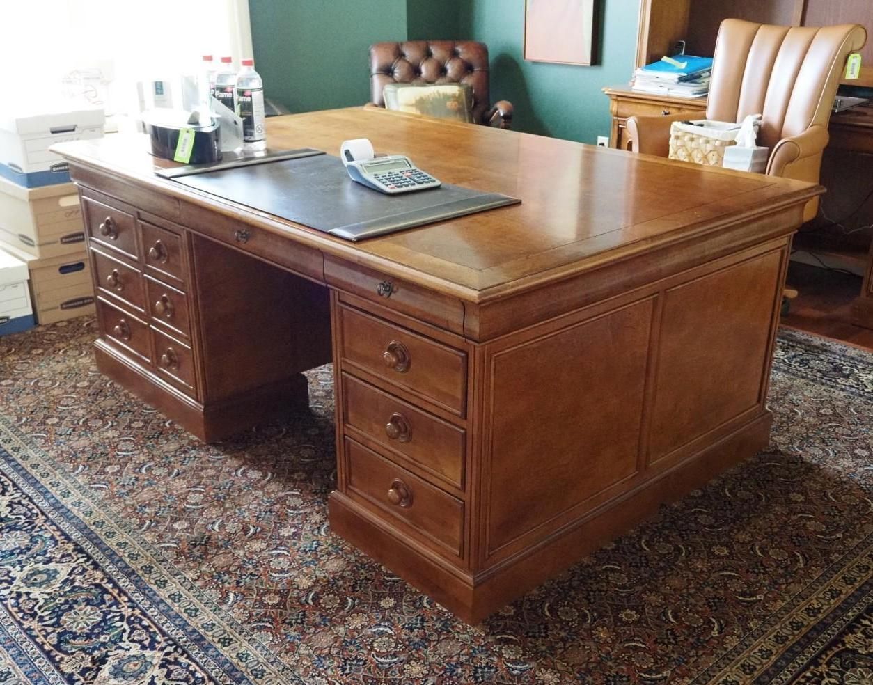 Large wooden desk with drawers and a leather writing surface, in a room with a patterned rug and furniture.