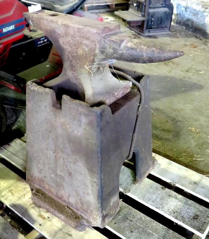 Anvil on a metal stand in a workshop setting. The anvil has a horn and flat surface.