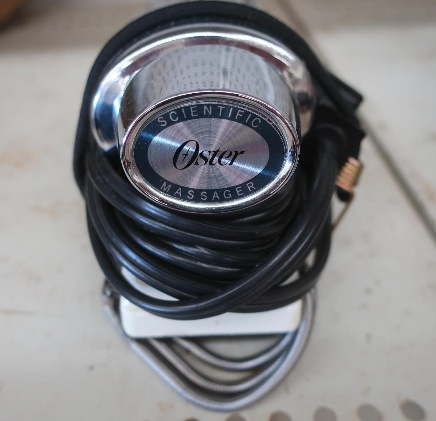 Oster Scientific Massager, chrome with blue oval logo, black cord wrapped around head.