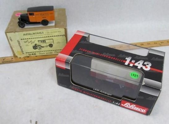Two model truck boxes, one with an orange truck, the other with a silver and black truck; ruler in background.