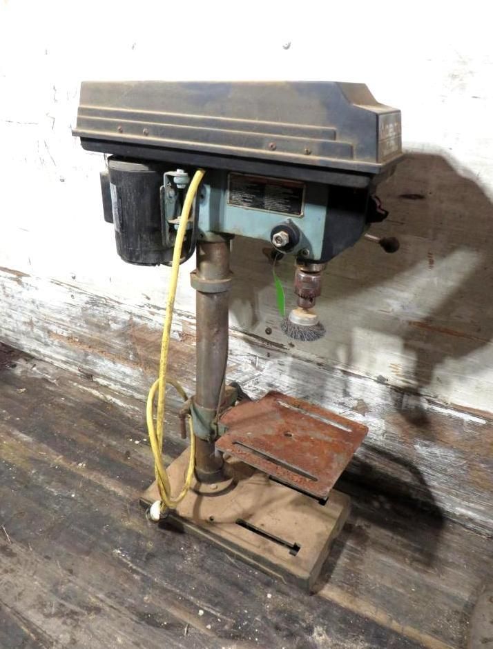 Drill press sits on a wooden base in a workshop, ready for use.