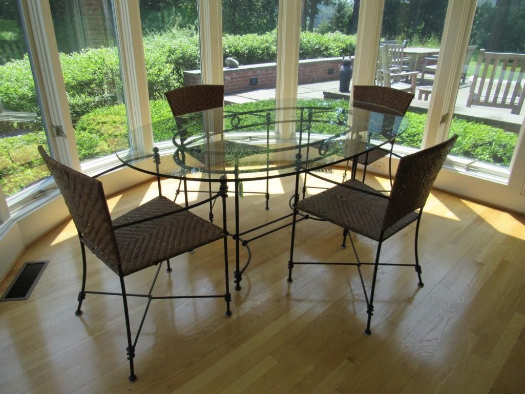 Glass table and four chairs in sunroom with views of greenery.