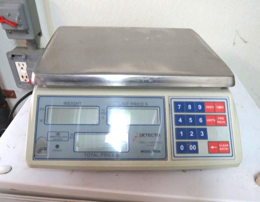 A digital retail scale with weight, unit price, and total price displays; keypad and stainless steel platform.