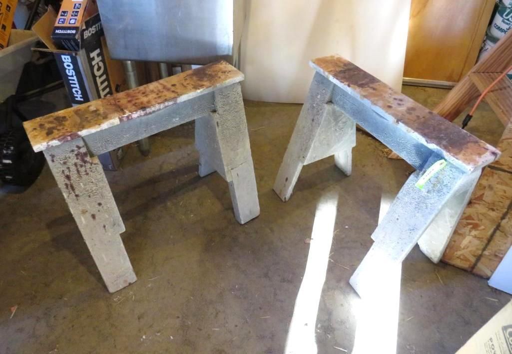 Two gray sawhorses on a concrete floor, with sunlight casting shadows.
