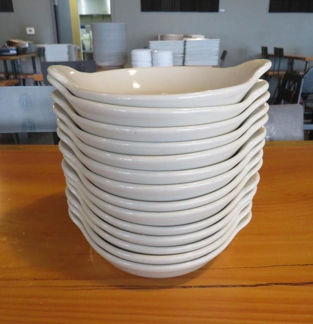 Stack of cream-colored, shallow serving bowls on a wooden surface, restaurant setting.
