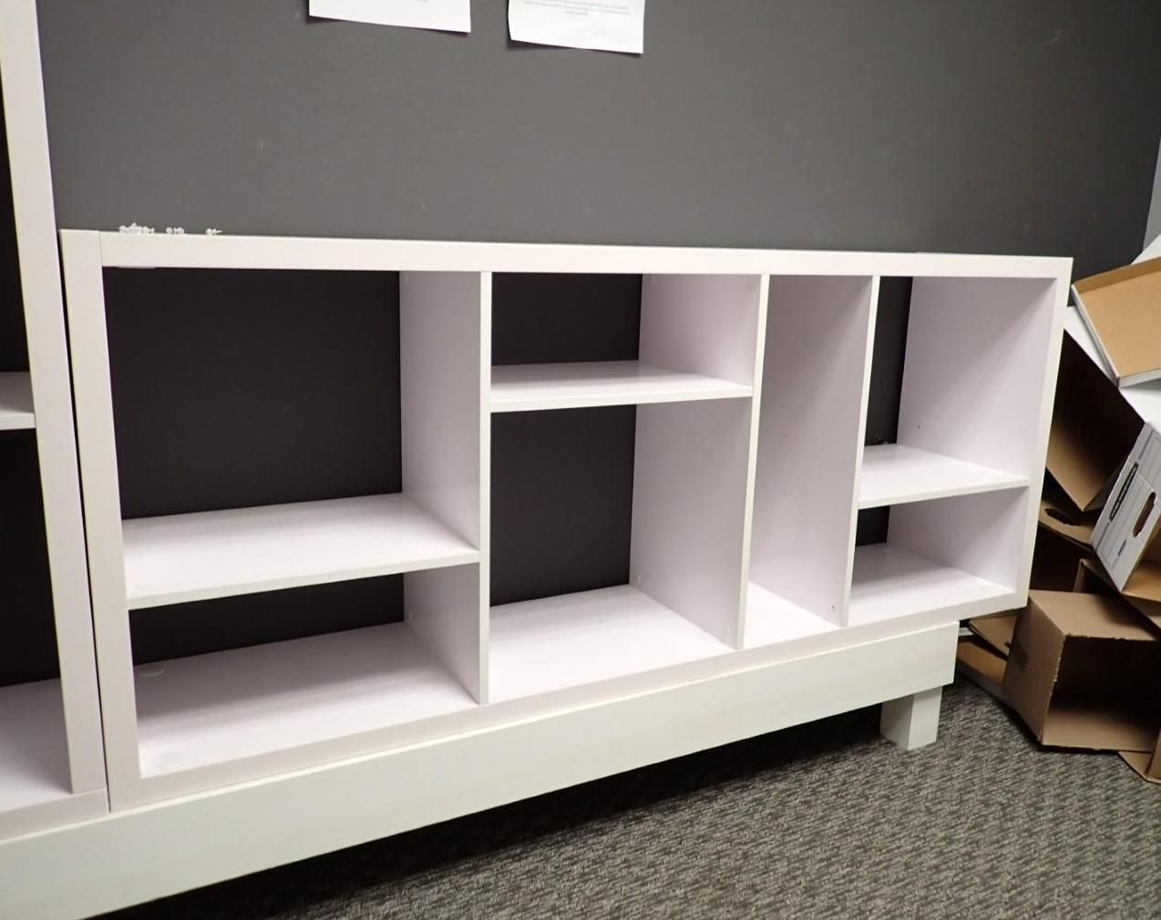 White storage unit with multiple shelves against a gray wall.