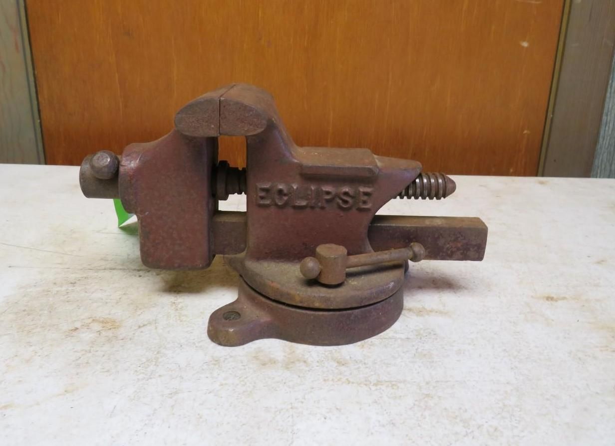 Brown Eclipse bench vise on a white surface, with a wooden backdrop.