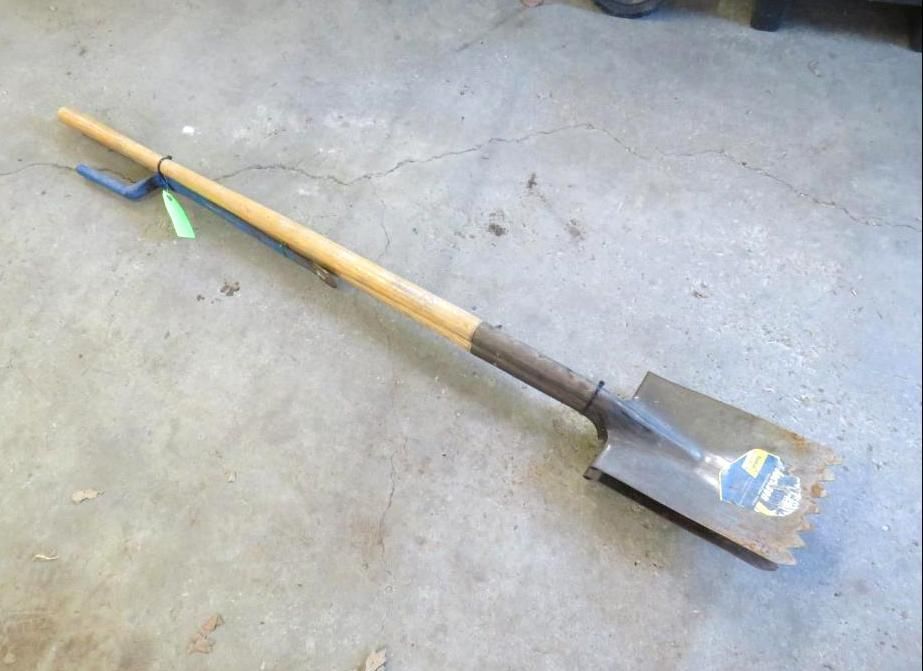 Long-handled shovel with a rectangular blade, laying on a concrete surface.
