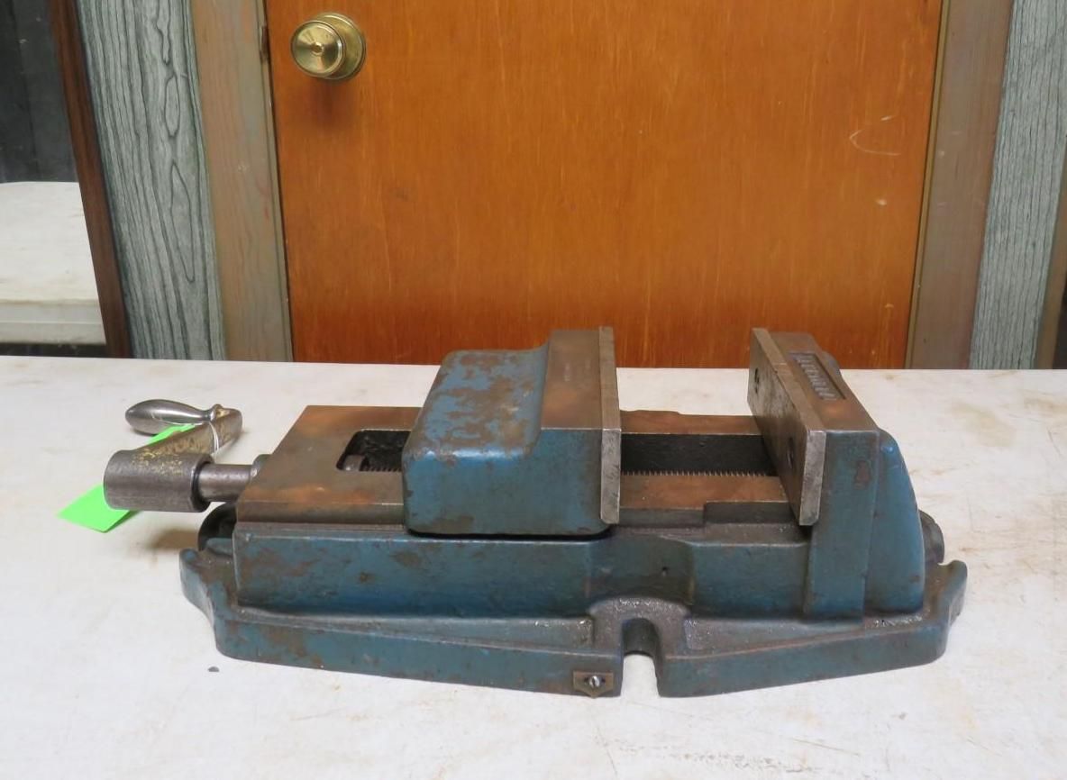 Blue and rusty metal bench vise on a work surface, handle on the left.