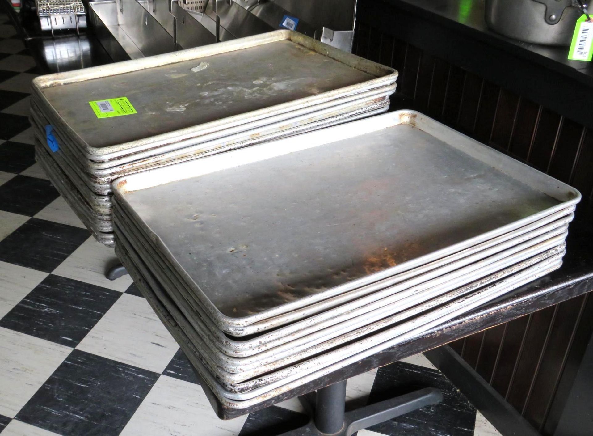Stacks of used aluminum baking sheets on a table with a checkered floor.