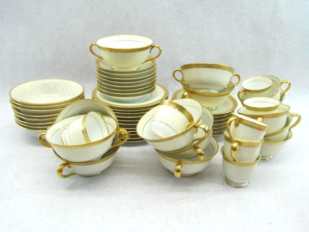 Cream-colored porcelain tableware set with gold trim, including bowls, cups, and plates, arranged on a white surface.