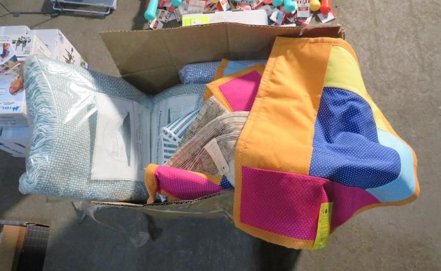 Open cardboard box filled with colorful items, including a patchwork fabric piece and wrapped pillows.