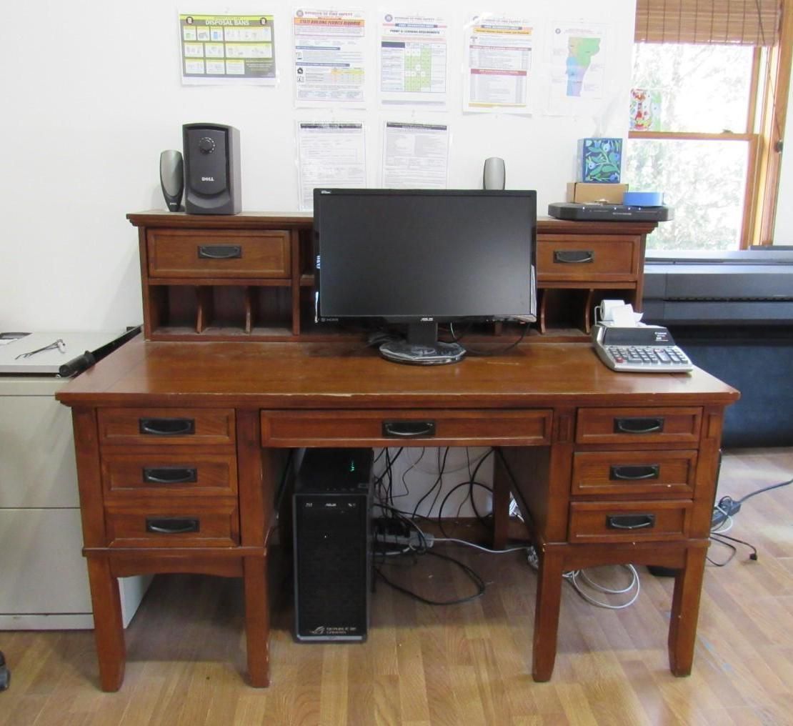 Wooden desk with drawers, computer, monitor, speakers, and office supplies.