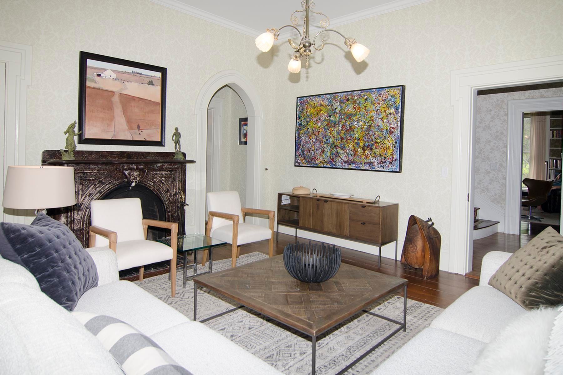 Living room with white sofa, chairs, fireplace, artwork, wood coffee table and sideboard.