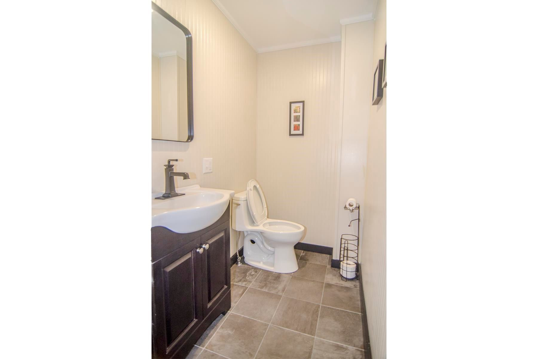 Small bathroom with a toilet, sink, and mirror. White walls and brown tile floor.