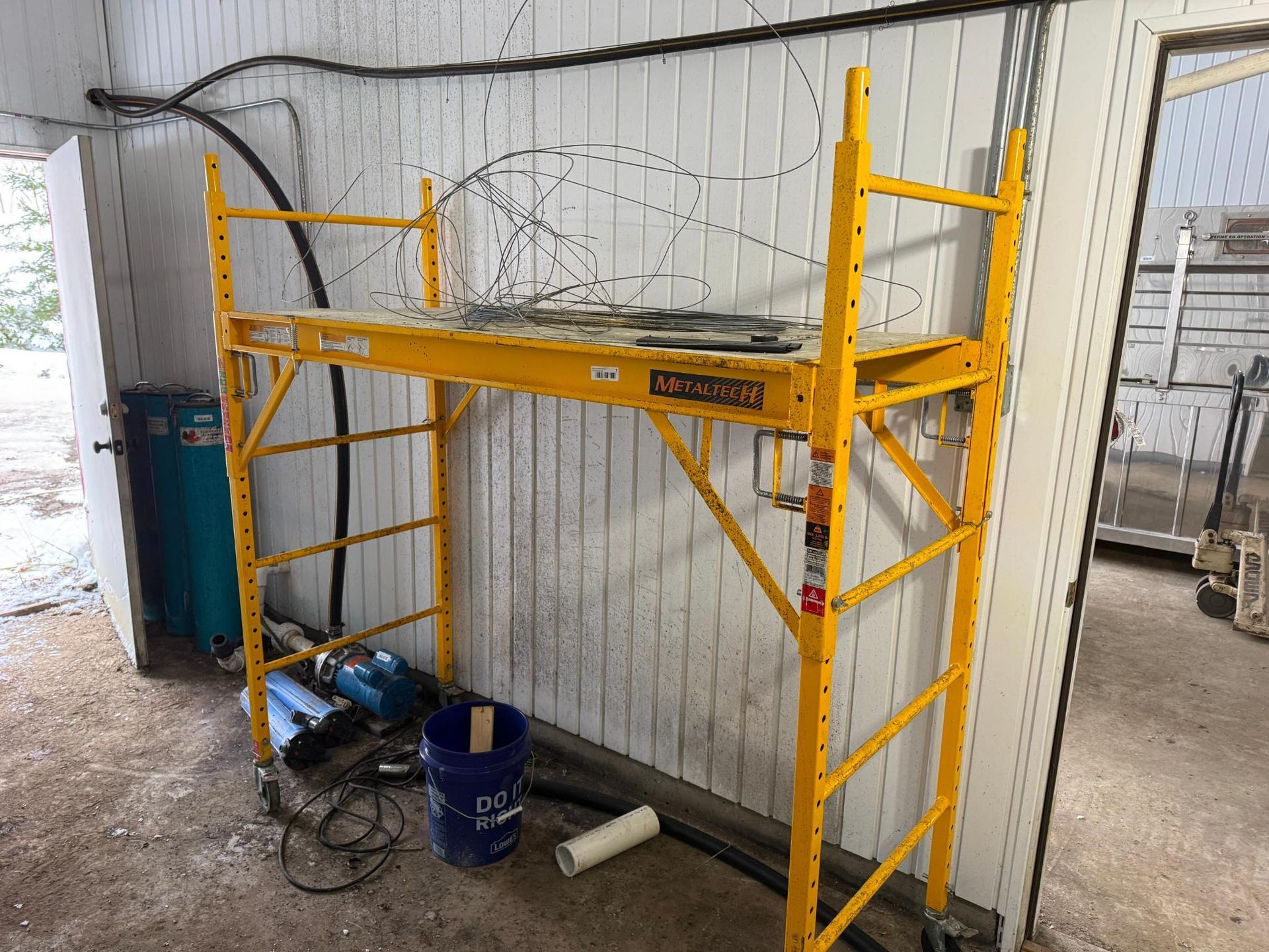 Yellow scaffolding inside a room, with tools and a bucket at the base.
