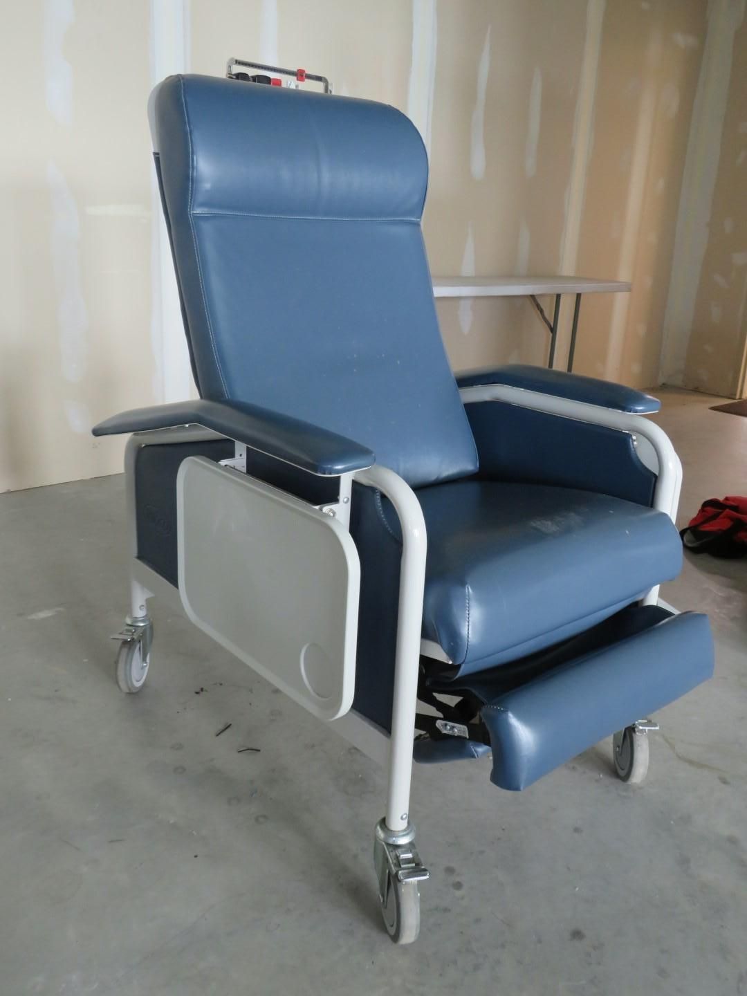 Blue medical recliner chair with a tray, on wheels.