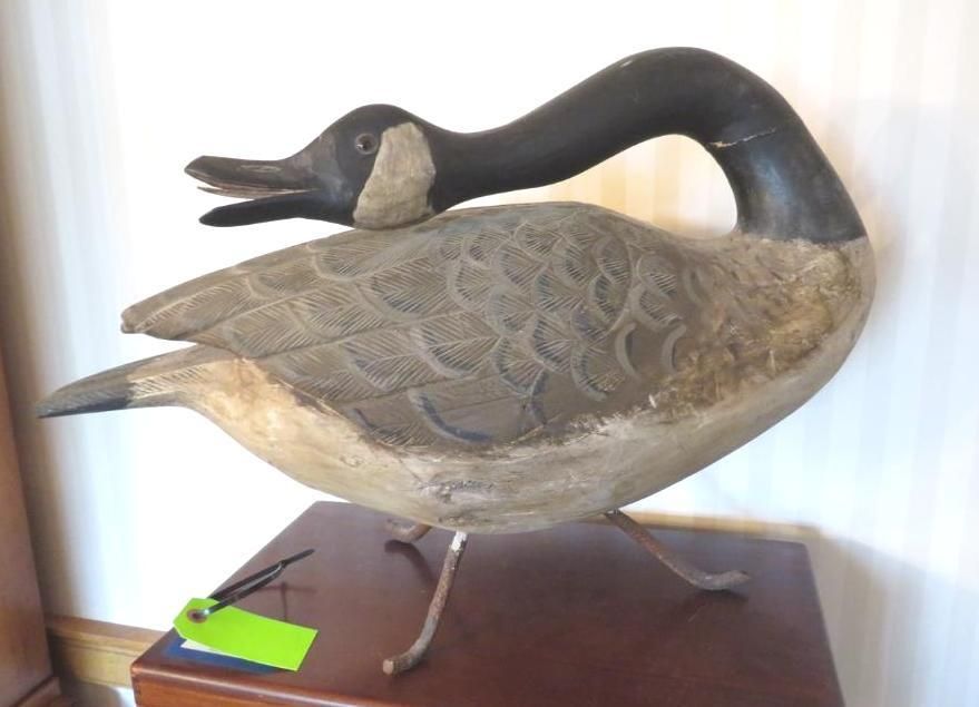 Wooden Canada goose decoy on a table, with open beak and metal legs.