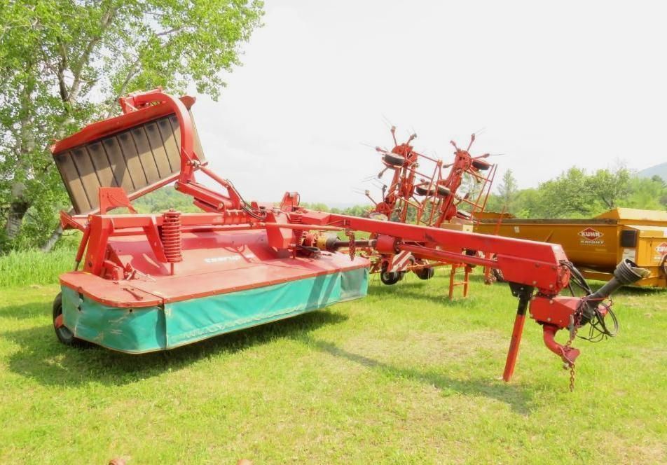 Red and green agricultural mower in a grassy field.